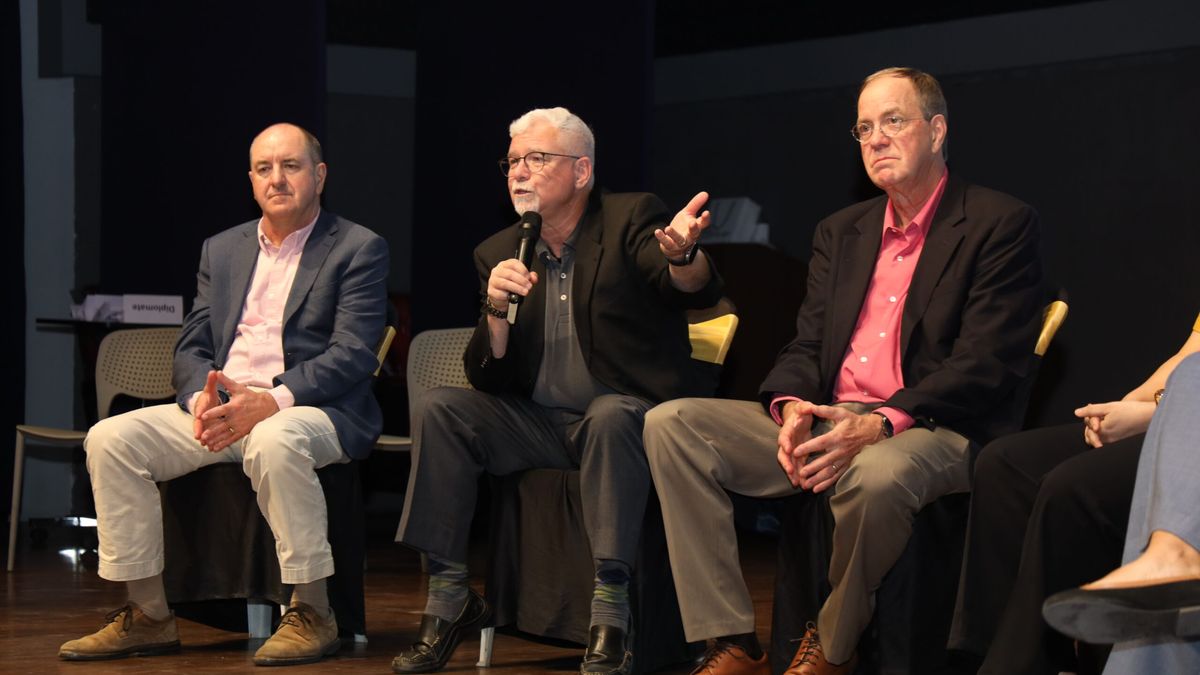 The three founders seated on stage, the one in the middle speaking into a microphone